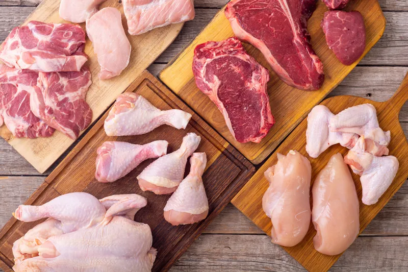 Assorted raw beef, pork and chicken cuts arranged on wooden boards